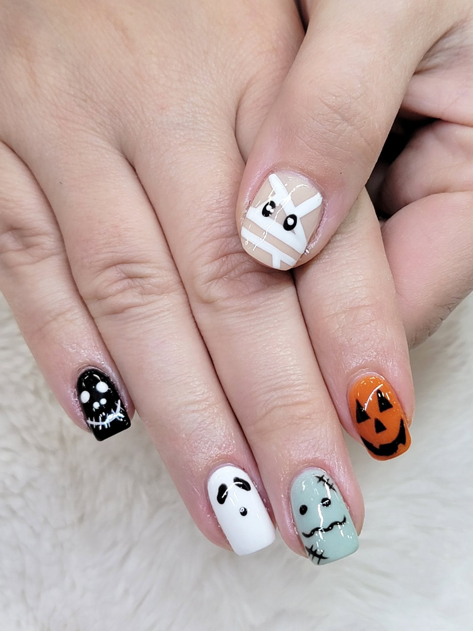 Playful Halloween themed nail art featuring pumpkin, ghost, Frankenstein, and mummy designs