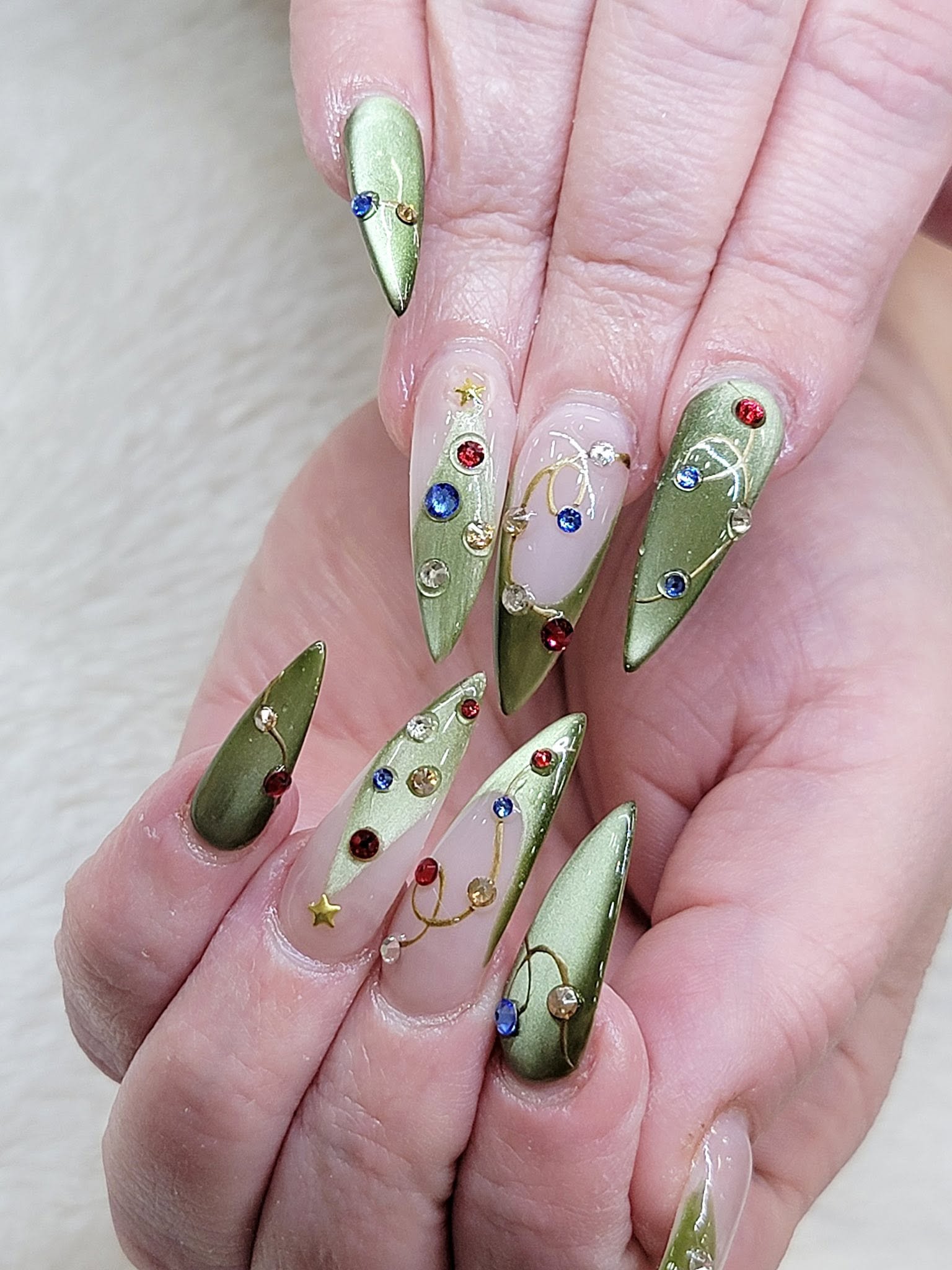 Metallic green chrome stiletto nails with hand-placed rhinestone holiday accents